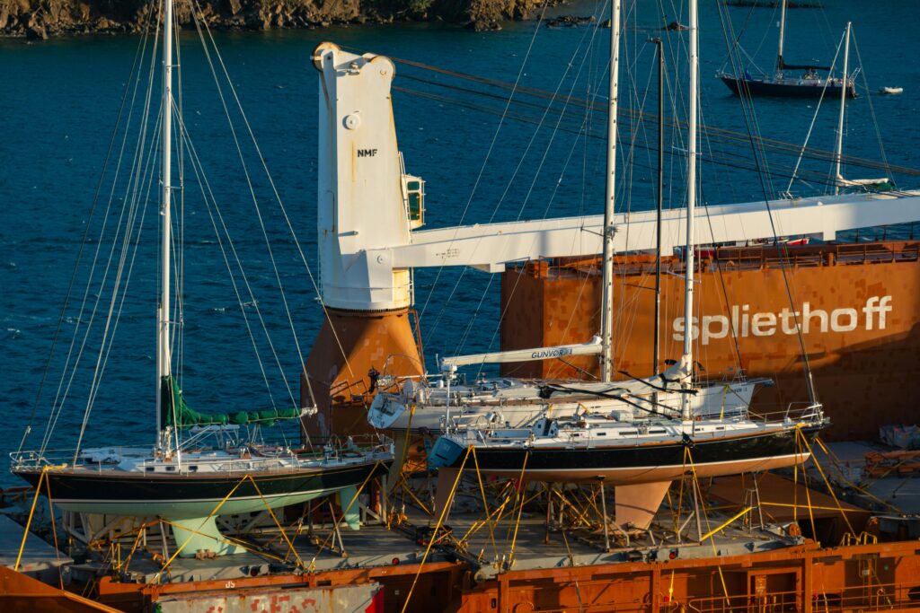 Sailing yachts securely placed on cargo ship deck in a sunlit harbor, ready for transport.