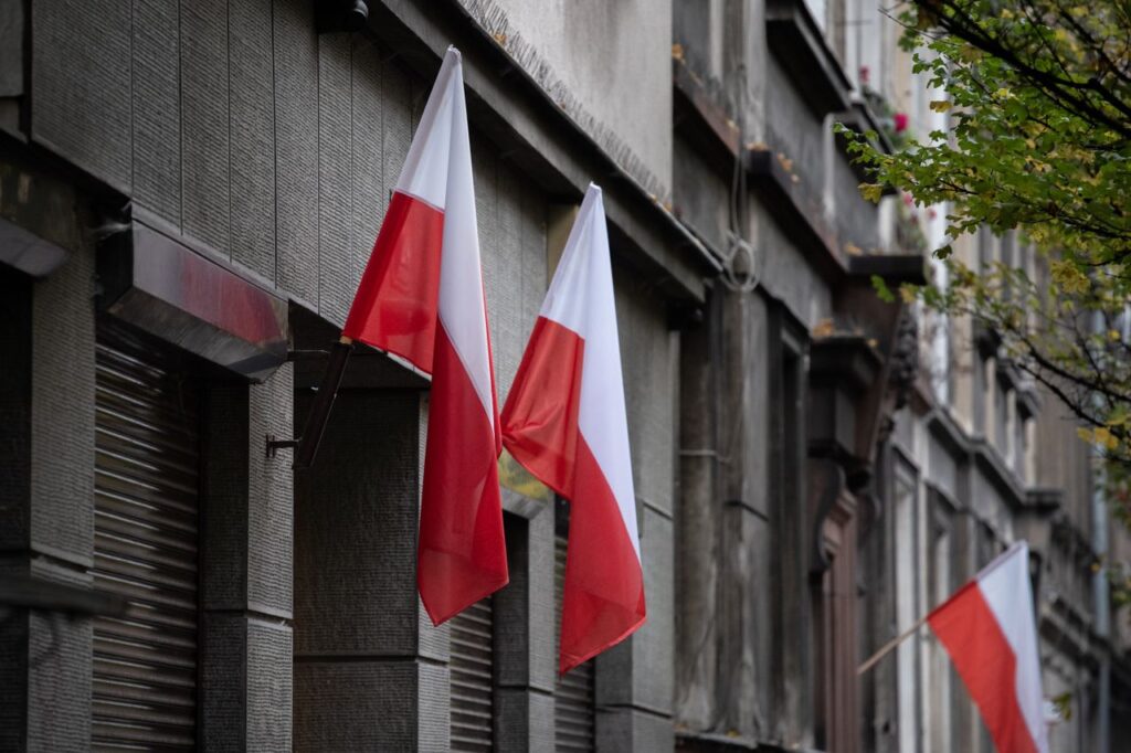 pexels-photo-19090937-19090937 Polish flags hanging on a historic urban building, symbolizing national pride.