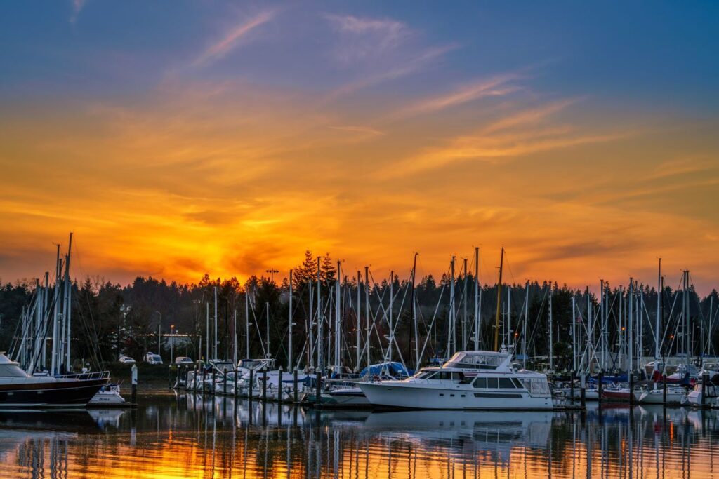 Experience a vibrant sunset over a peaceful marina with boats and yachts reflecting on tranquil waters.